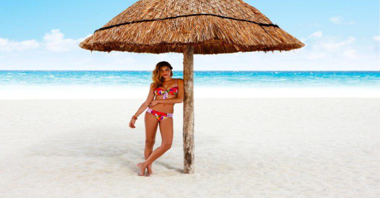Mujer joven en traje de baño en la playa bajo una palma