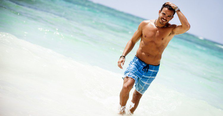 Hombre musculoso caminando a la orilla del mar turquesa de día