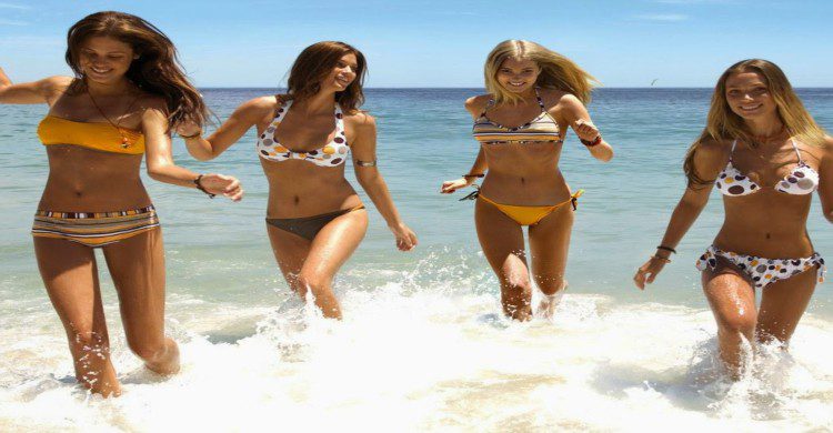 Cuatro mujeres en traje de baño saltando a la orilla del mar