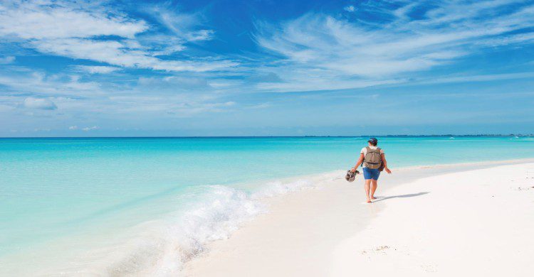 Persona caminando en playa caribeña de Santiago, Cuba con arena blanca y mar turquesa
