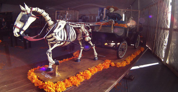 Escultura de hombre conduciendo una carreta con caballo calavera