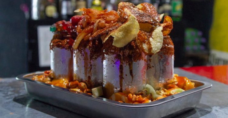 Latas de cerveza en una charola con papas, gomitas y cacahuates